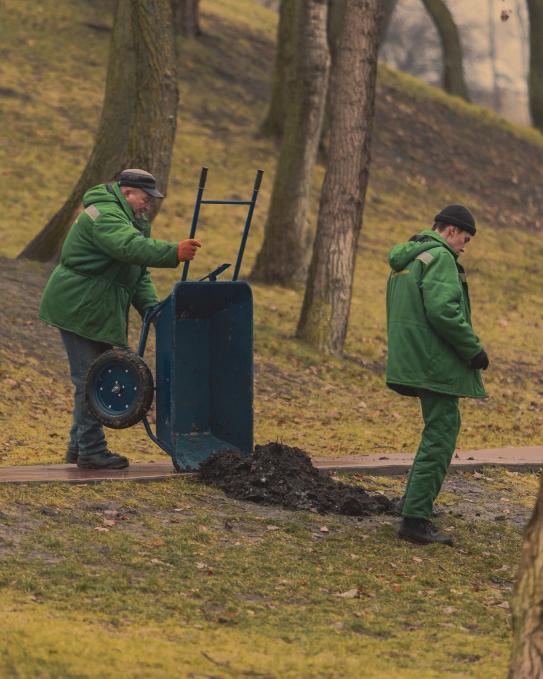 Grounds crew at work with a wheelbarrow among fall leaves