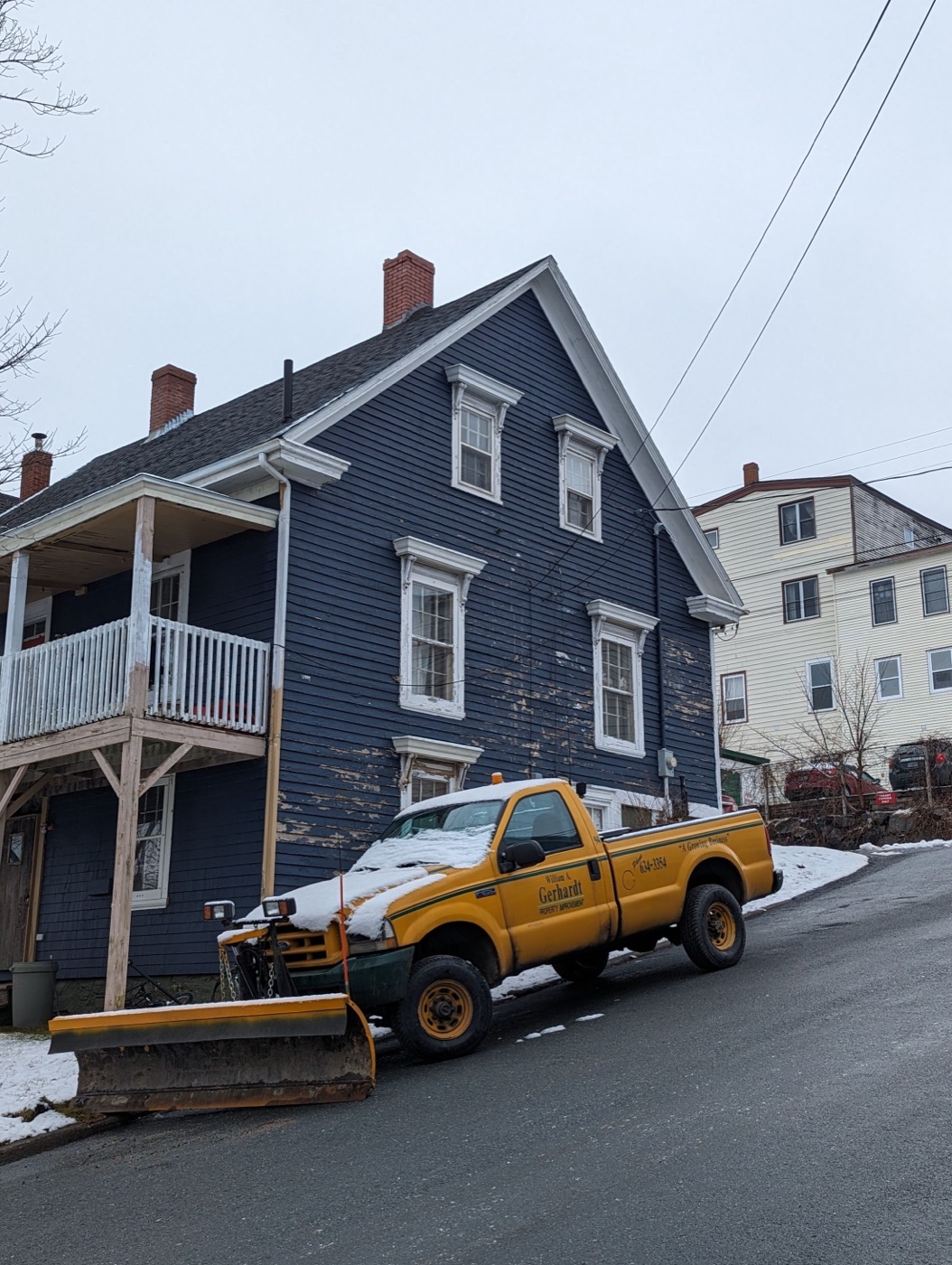 Plow truck working a snowy street of wooden houses