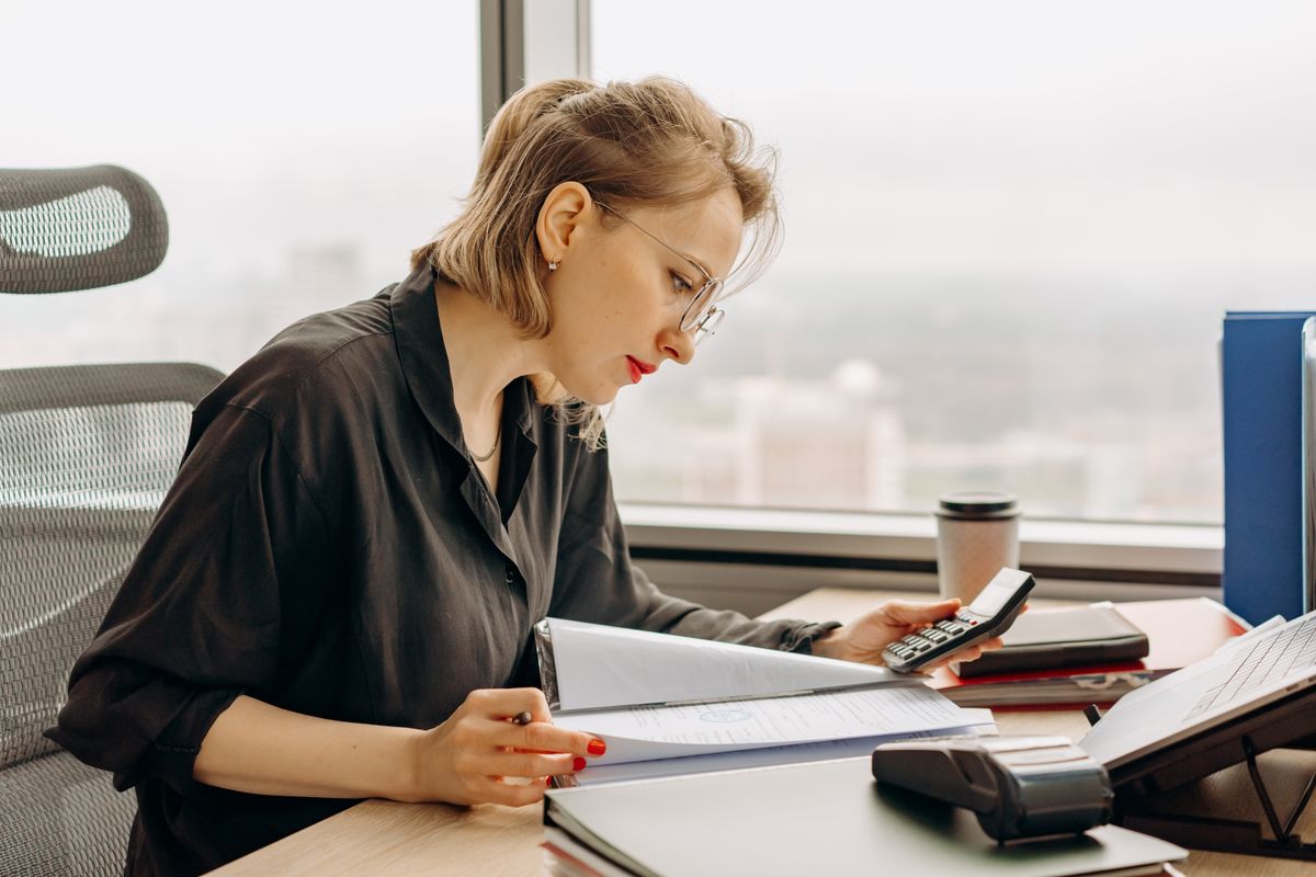 Financial administrator working through a stack of ledgers with a calculator