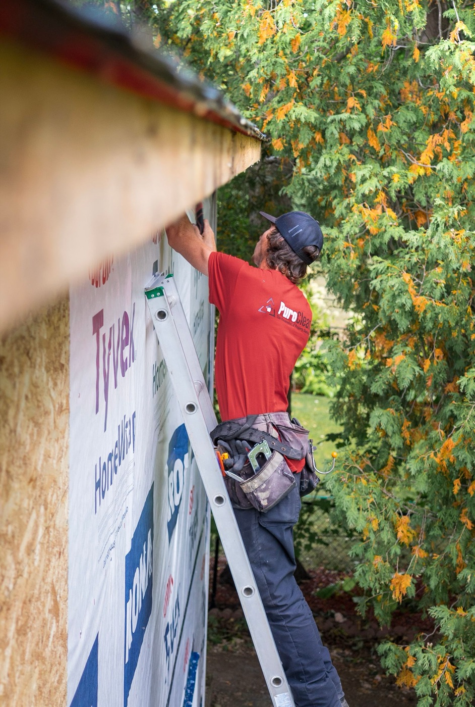 Worker on a ladder repairing siding on a clapboard house